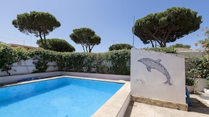 A swimming pool with a dolphin mosaic, surrounded by trees and a white wall.