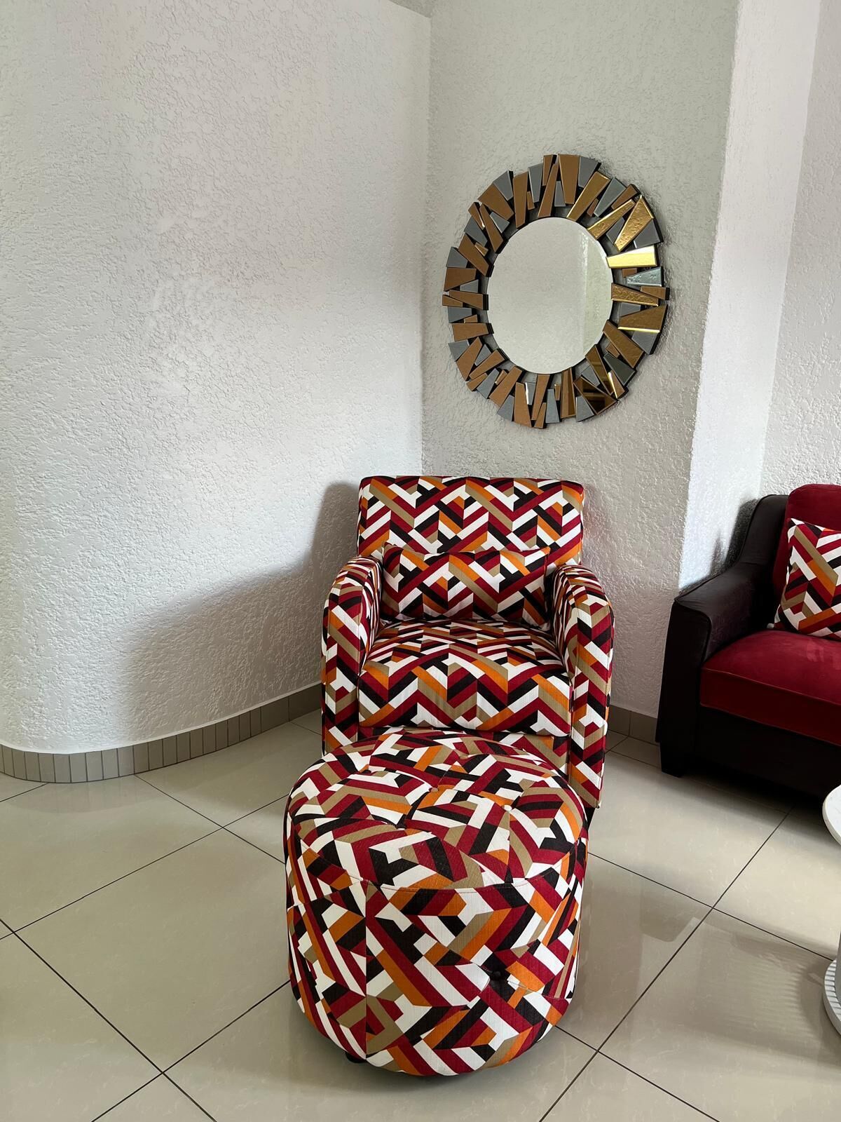 A modern living room with a patterned armchair, a round mirror, and a red sofa.