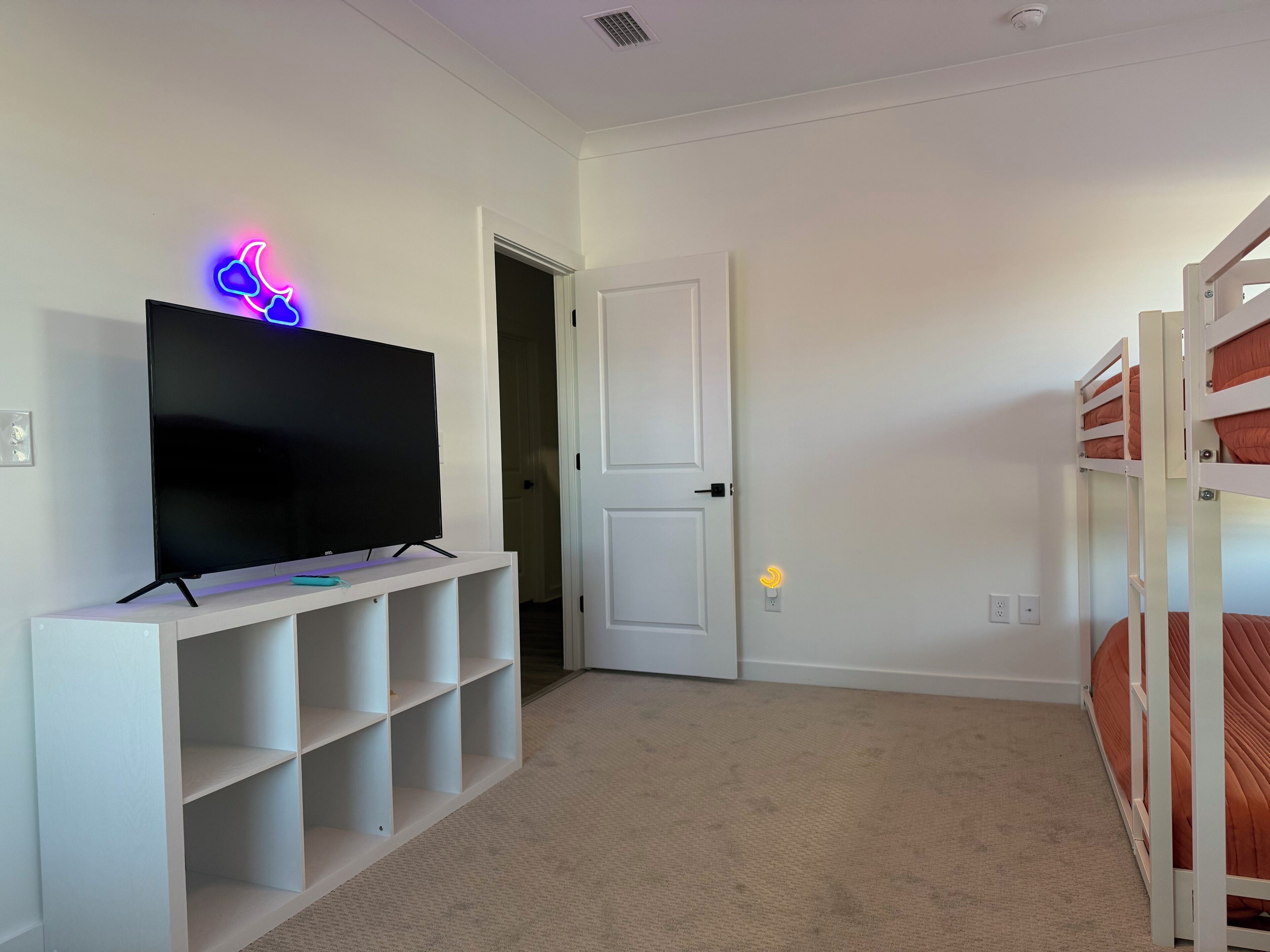 A room with a TV on a white stand, a door, and bunk beds.