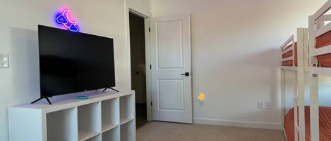 A room with a TV on a white stand, a door, and bunk beds.