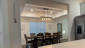 A modern kitchen with a large island, wooden dining table, and chairs. There is a hanging light fixture above the island and a refrigerator on the right. - Large Family Friendly 4BR/10 Bed. Pool, Bay Access (Orange Beach)