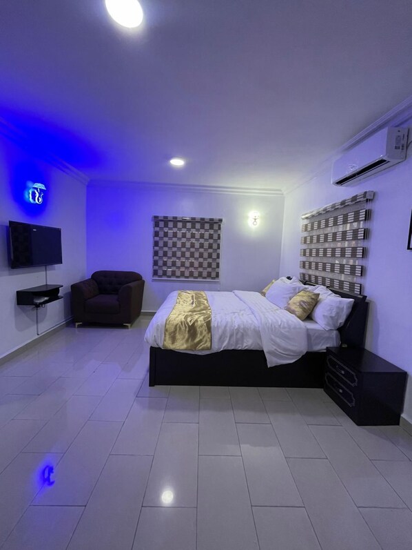 A modern bedroom with a bed, a chair, a TV, and a wall-mounted air conditioner.