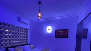 A bedroom with a bed, a nightstand, a wall-mounted light, and a mirror. - Trans Amadi Gardens Duplex (Port Harcourt)