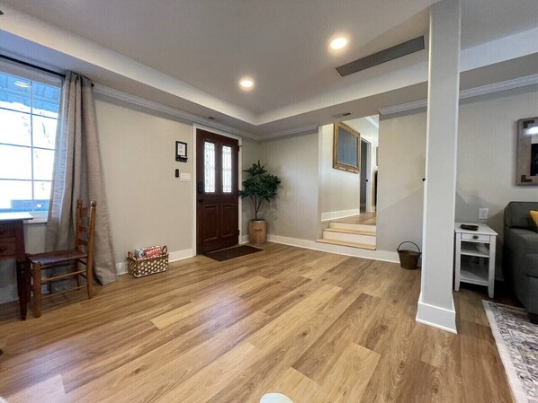A spacious living room with hardwood flooring, a dining area with a wooden table and chairs, a staircase leading to another level, and a grey sofa.