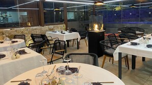 Un restaurant amb taules preparades per dinar, una llar de foc central i un mur de pedra de fons.