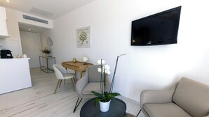 Un saló modern amb un sofà, una taula de centre i una televisió. Hi ha una zona de dinar amb una taula i cadires, i una cuina amb una màquina de cafè.