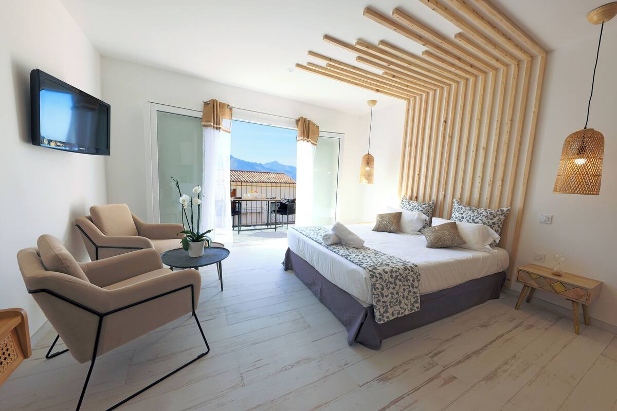 A modern bedroom with a bed, two chairs, a small table, and a TV.