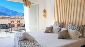 Habitació d'hotel amb llit, almoines, llum penjant i balcó amb taula i cadires.