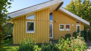 Un bâtiment jaune avec un toit en pente, une porte et trois fenêtres.