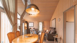 L’intérieur d’un chalet accueillant, avec une table à manger en bois, des chaises, un canapé et un grand luminaire suspendu.