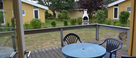 Una terraza con una mesa redonda y sillas, con vistas a un patio trasero que incluye una parrilla y un edificio amarillo.