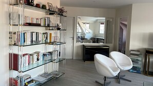 Un salon moderne avec une bibliothèque en verre, un fauteuil blanc et un escalier menant à une autre pièce.