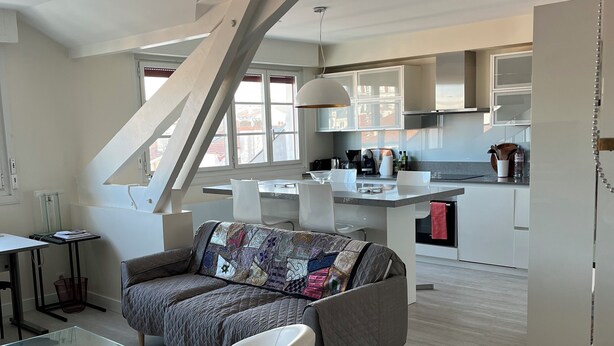 Un espace de vie moderne comprenant un canapé, une table basse en verre, une chaise blanche et un coin cuisine avec des placards et une table à manger.