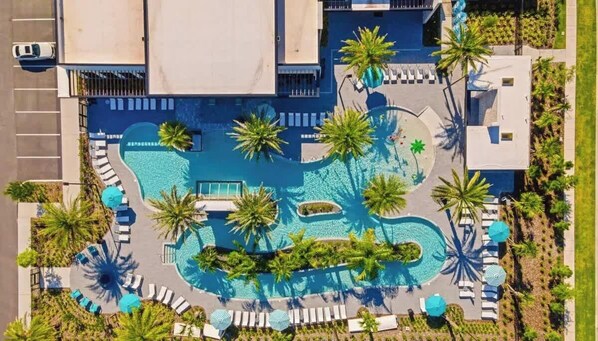 An aerial view of a hotel with a central swimming pool surrounded by palm trees and lounge areas.