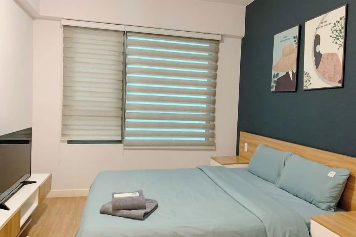 Quarto com cama, televisão, janela com persianas e duas obras de arte na parede.