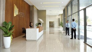 Ein moderner Hotel-Empfangsbereich mit Holzbüro, einer Rezeptionistin und zwei wartenden Gästen.