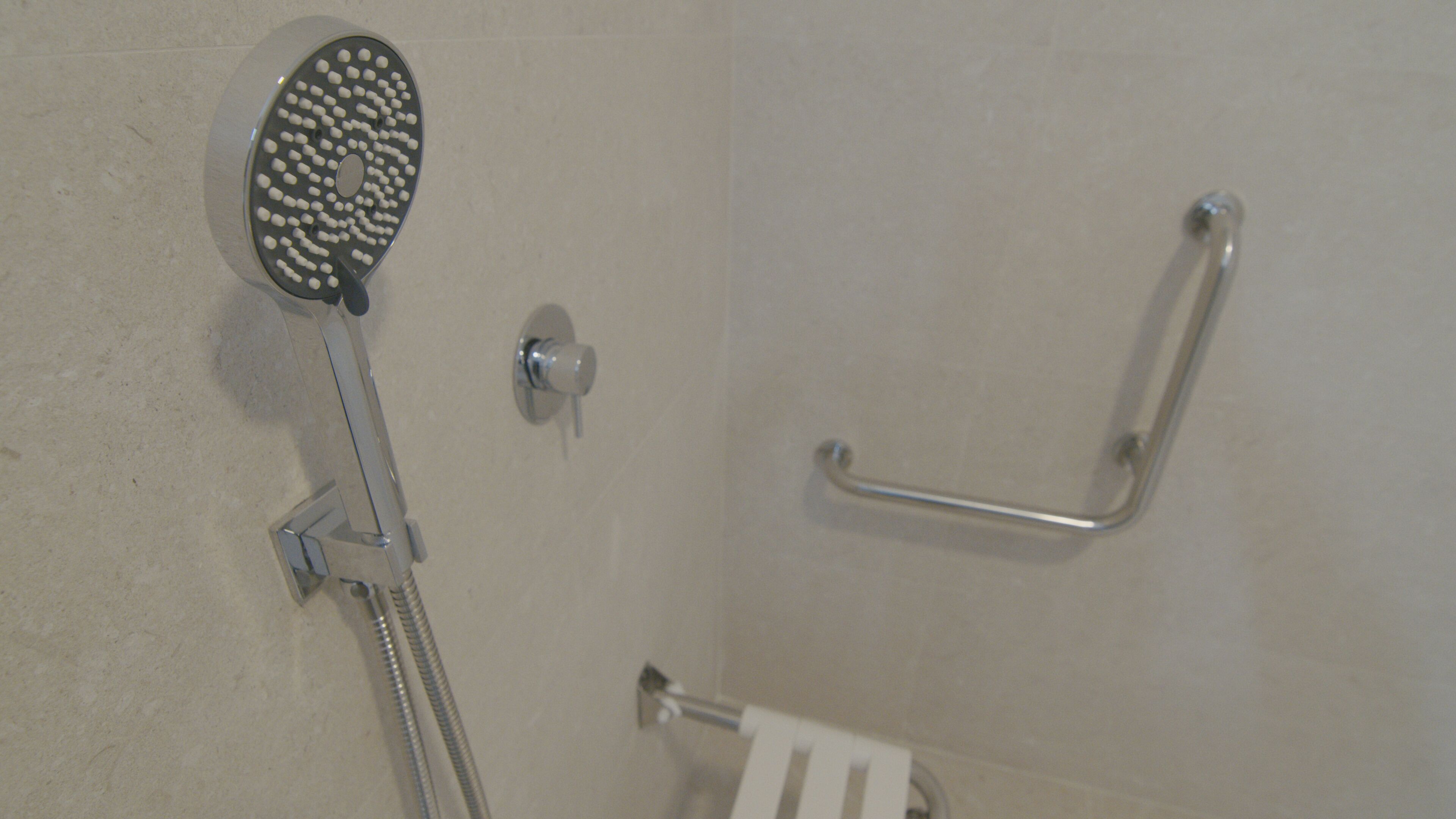 A shower with a handheld showerhead and a grab bar.