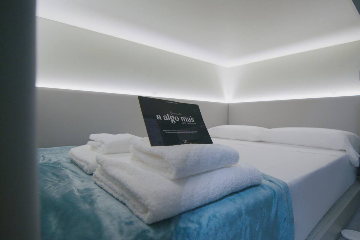 A hotel room with a neatly made bed, a stack of towels, and a sign on the wall.