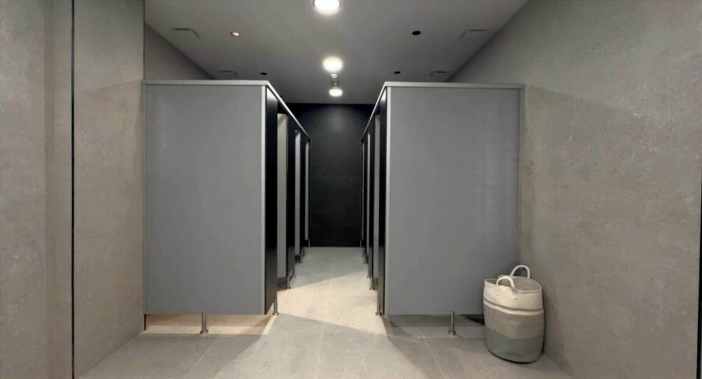 A corridor with multiple restroom stalls and a trash bin.