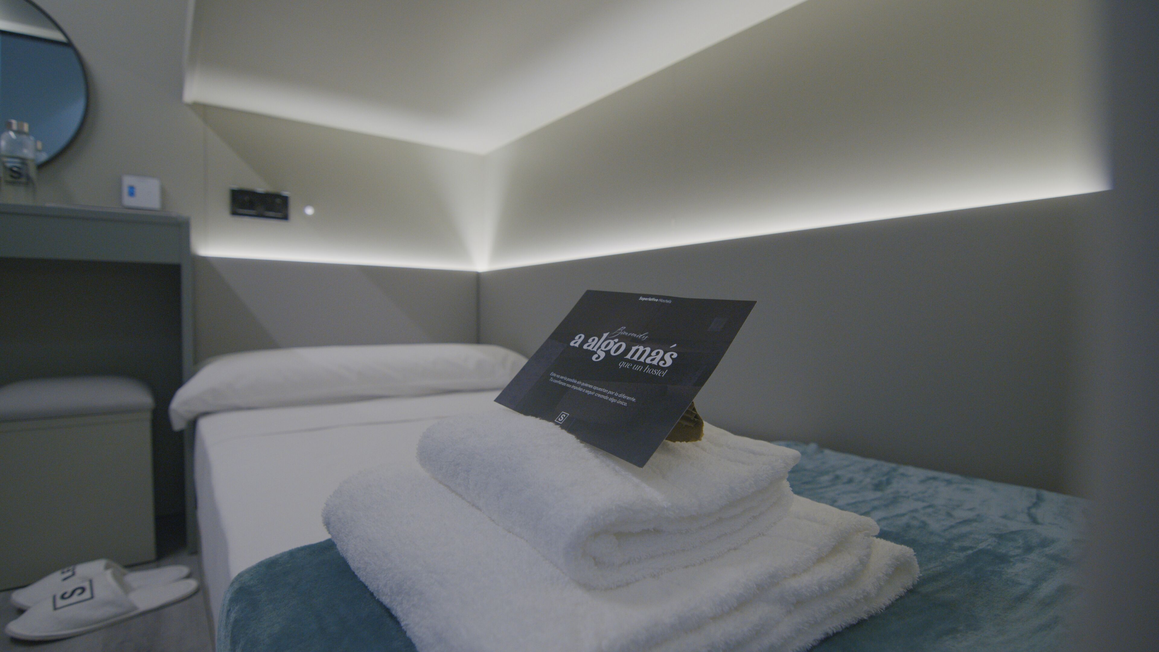 Una cama bien hecha con una toalla doblada y un libro titulado "A algo mas que un hostal" encima.