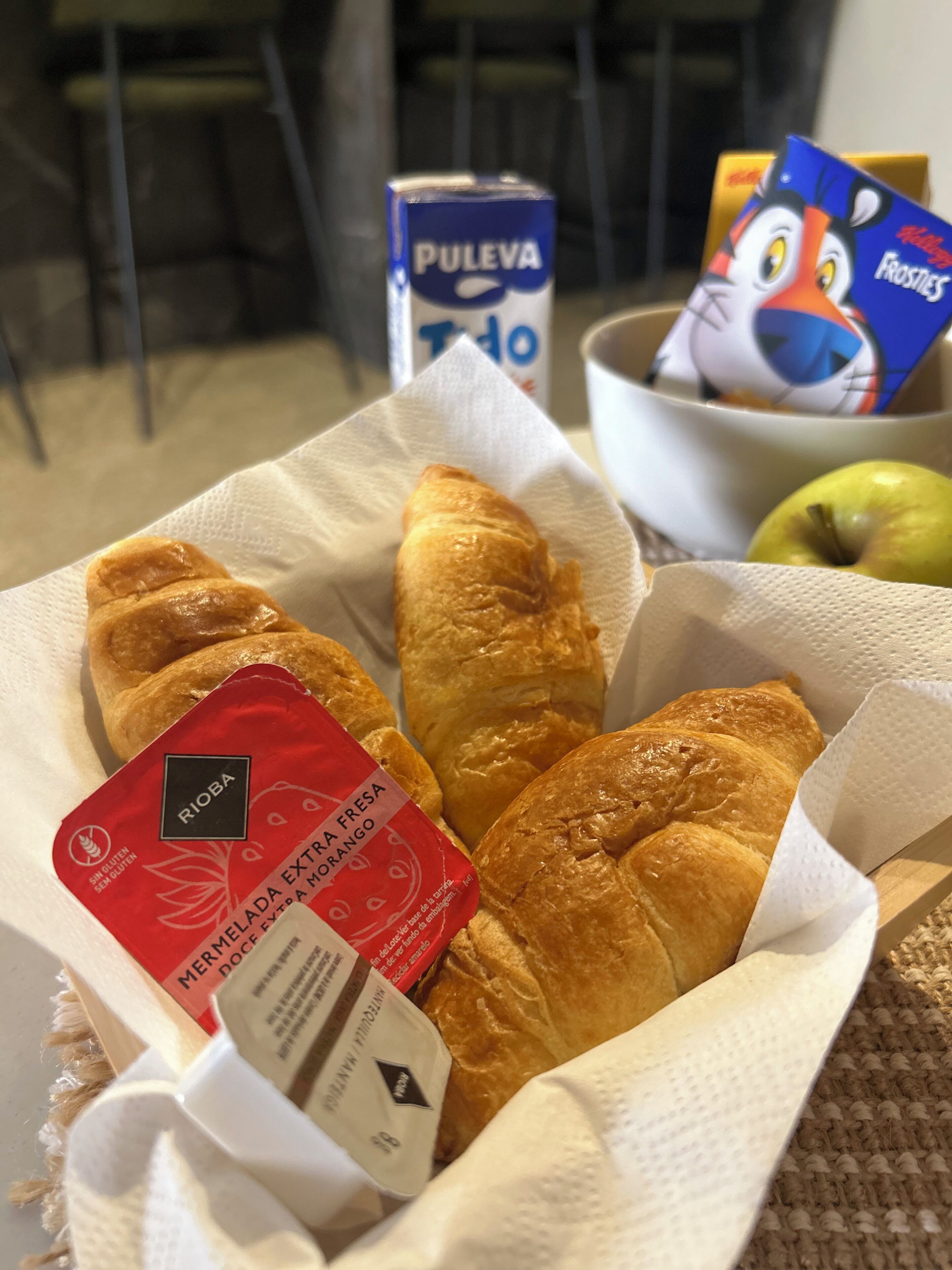 A tray with croissants, a box of Pulao, a box of Frosties, and a green apple.