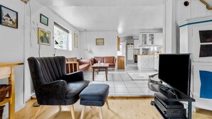 A modern living room with a black leather sofa, a wooden coffee table, and a flat-screen TV. There is a kitchen area with white cabinets and a marble countertop. - Lovely home in Grevinge with WiFi (Grevinge)