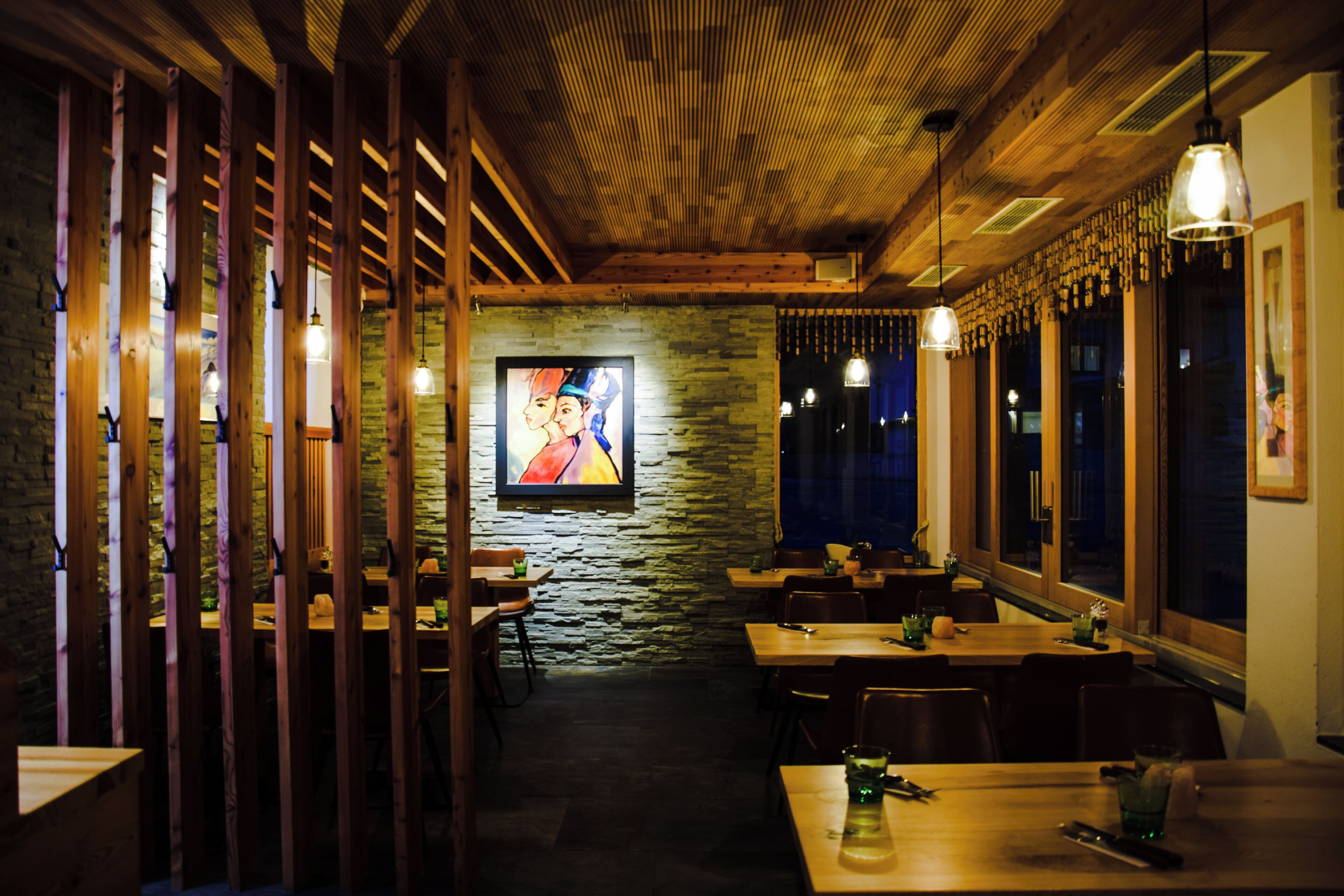 Un restaurante con vigas de madera, paredes de piedra y lámparas colgantes. Las mesas están dispuestas para comer.