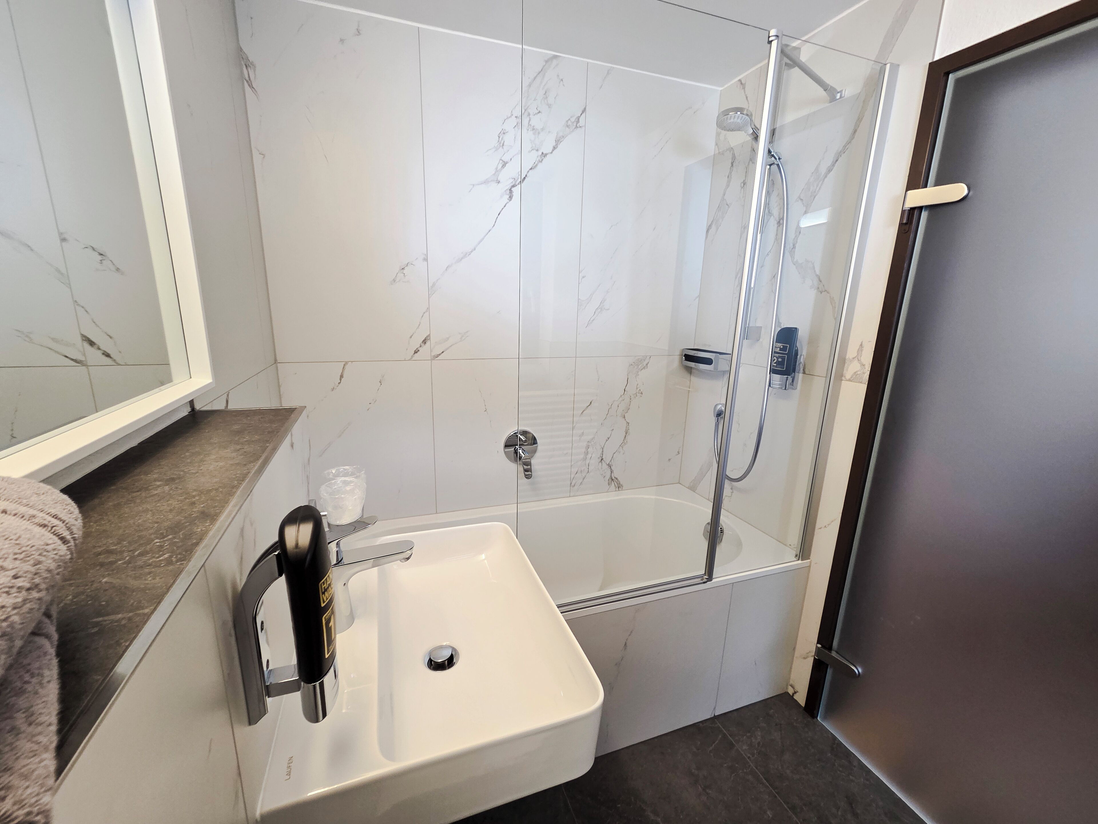 Une salle de bain avec un lavabo blanc, une douche en verre et des murs à motifs de marbre.