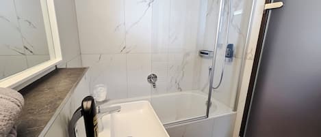 Une salle de bain avec un lavabo blanc, une douche en verre et des murs à motifs de marbre.