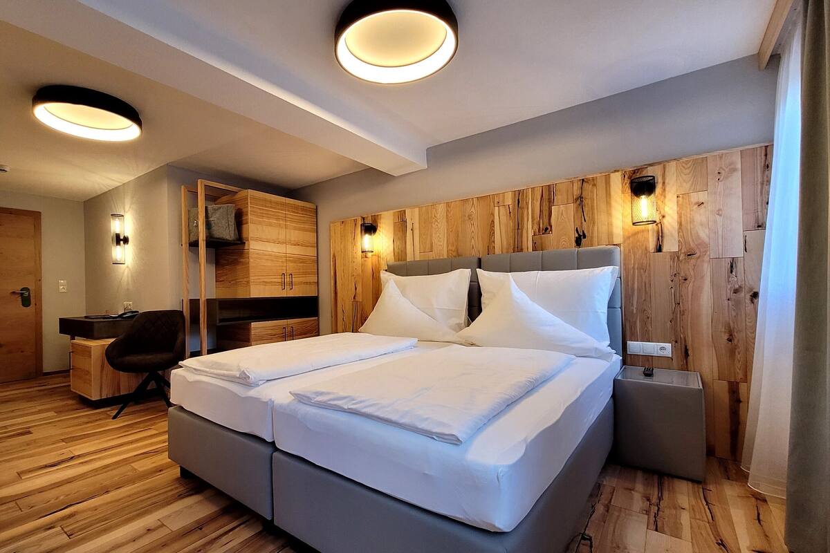 A modern hotel room with a large bed, wooden panel walls, and built-in lighting.