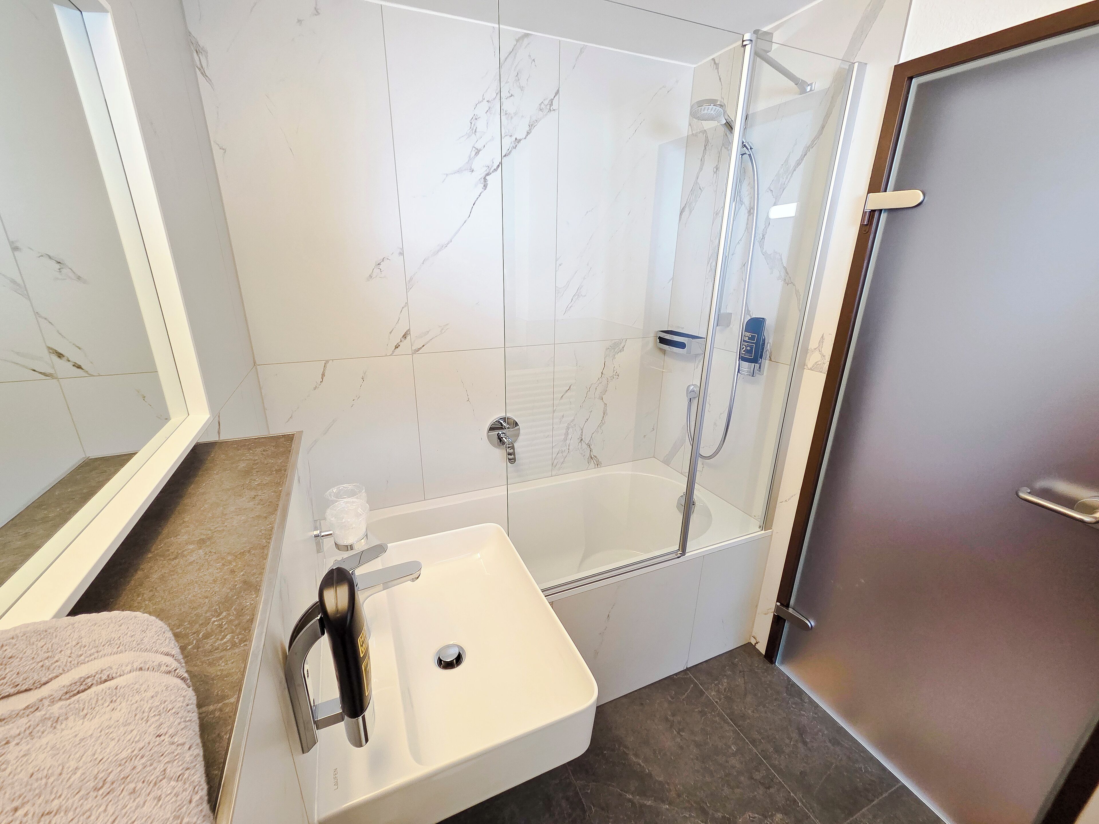A bathroom with a white sink, a glass-enclosed shower, and marble tiles.