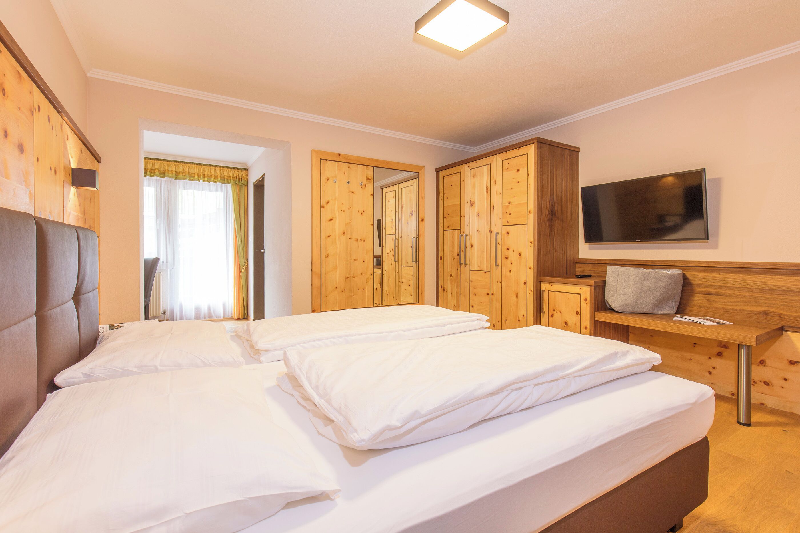 Ein Hotelzimmer mit zwei Betten, einem Holzschrank, einem Fernseher und einem Fenster mit Vorhängen.