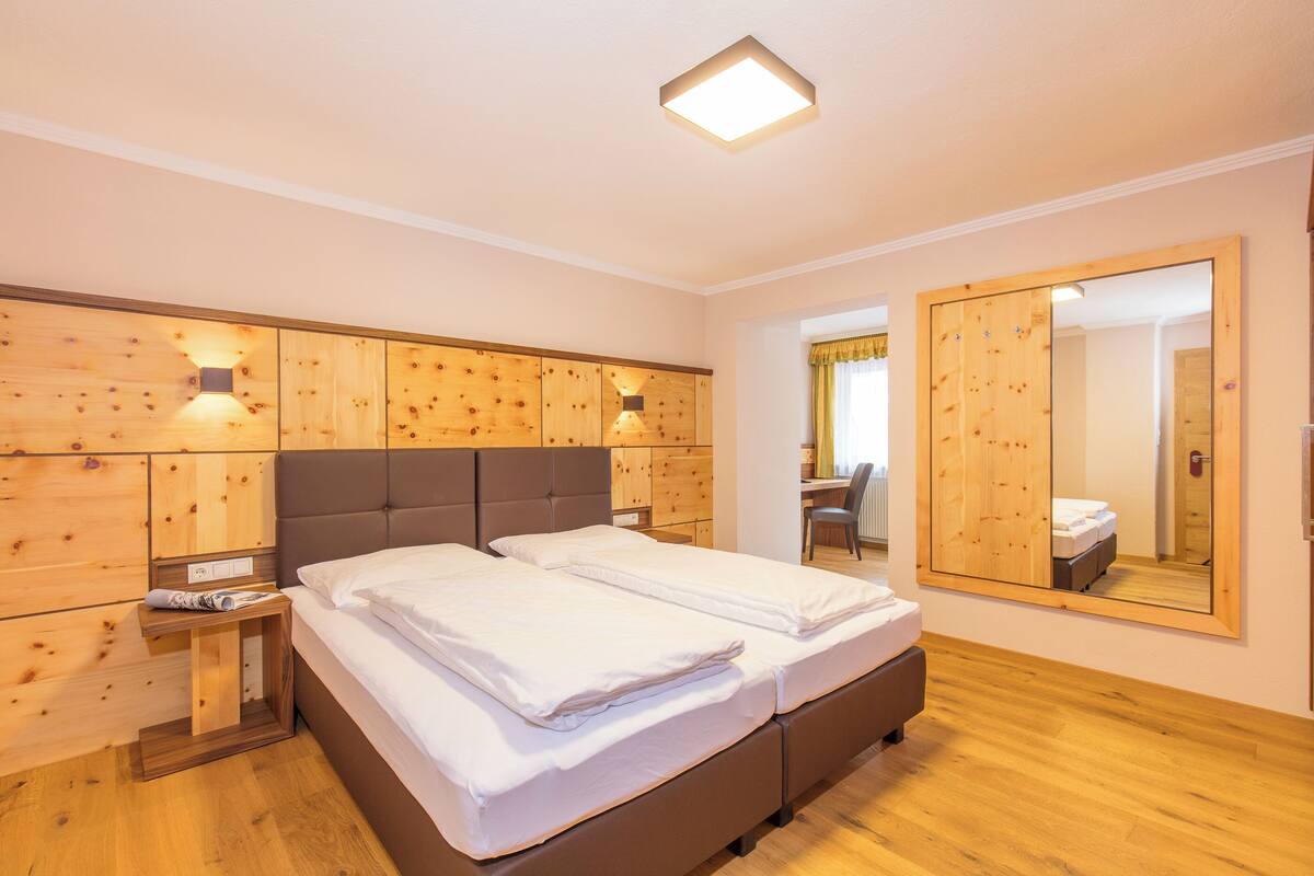 A bedroom with a wooden headboard, a large mirror, and a bedside table with a lamp.