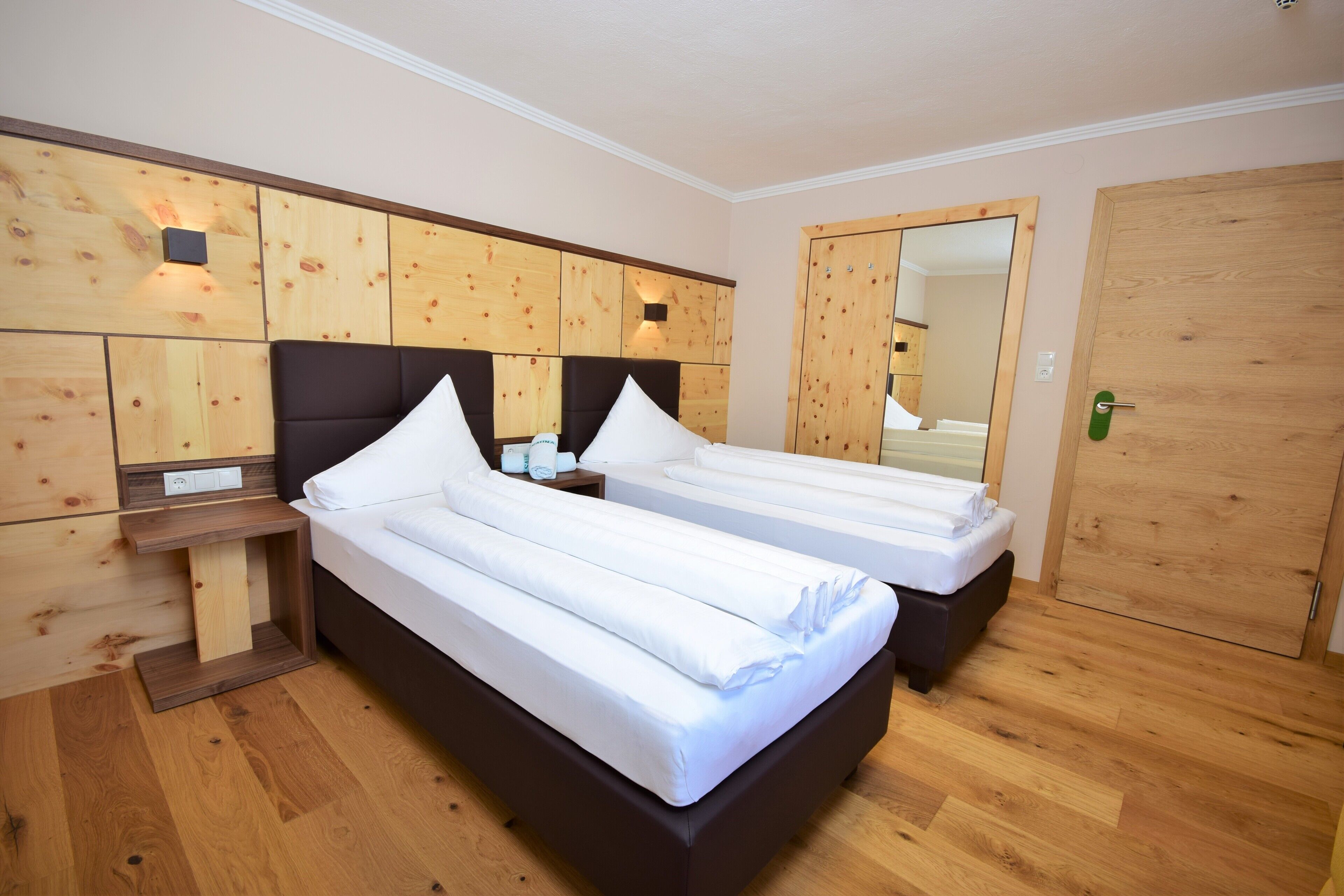Een hotelkamer met twee enkele bedden, houten hoofdeinden, een houten garderobe en een spiegel.