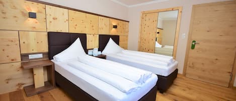 Een hotelkamer met twee enkele bedden, houten hoofdeinden, een houten garderobe en een spiegel.