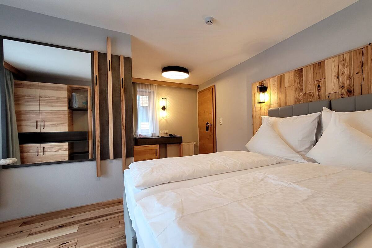 A modern hotel room with a large bed, wooden headboard, and a built-in wardrobe.