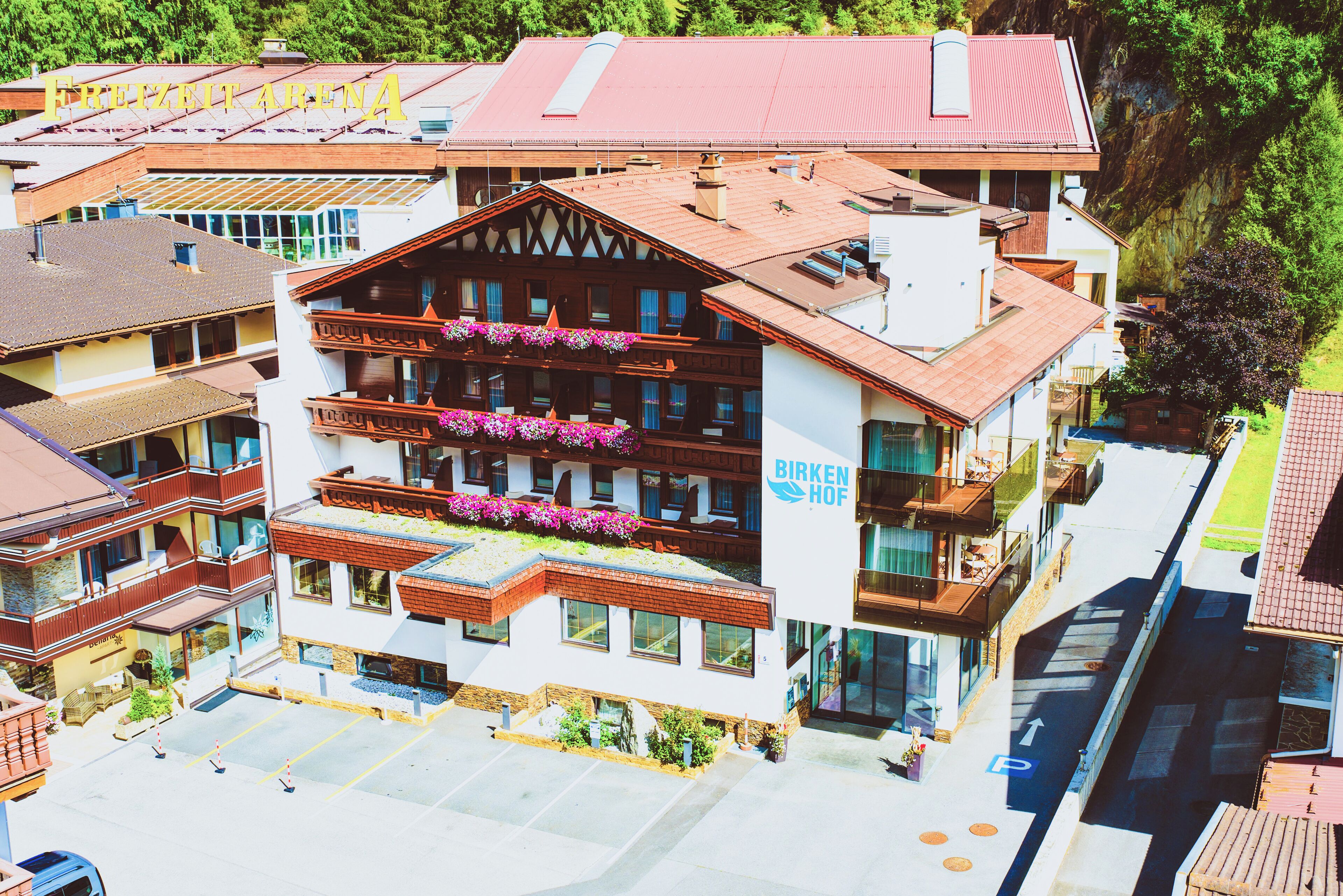 Un hotel de varios pisos con balcones, un estacionamiento y un letrero que dice 'Birkenhof'.