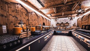 A modern kitchen with wooden accents, a central island with various food items, and a hexagonal tile floor. - Hotel Birkenhof (Soelden)