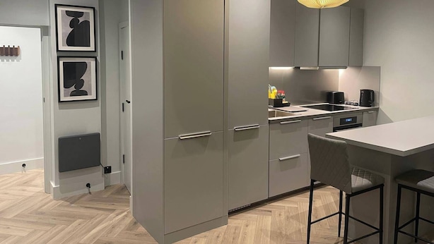 A modern kitchen with grey cabinets, a built-in oven, and a bar area with stools.