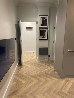 Stylish hallway with herringbone-patterned floor, framed artworks, and a door leading to another room.