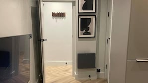 A hallway with a door leading to a room, a wall-mounted heater, and two framed abstract art pieces.
