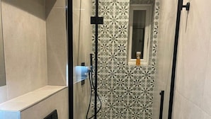 A shower area with a glass door, a window, and a patterned tile wall.