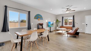 A spacious living area with a wooden dining table, white chairs, a brown leather sofa, and a TV mounted on the wall. - A-Mountain Wonder! HUGE yard, dogs OK - Brand New everything Close to Downtown! (Tucson)