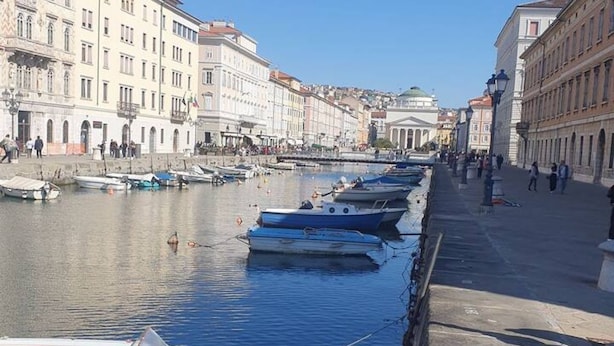 A waterfront promenade with boats docked along the side, a clear sky, and historic buildings in the background. - Trieste Central Holiday Home (Trieste)