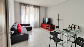 A modern living room with a sofa, red entertainment unit, glass dining table, and a TV. - Trieste Central Holiday Home (Trieste)