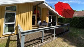 Ein gelbes Haus mit einer Holzdiele, einem roten Sonnenschirm und einem Tisch mit Stühlen.