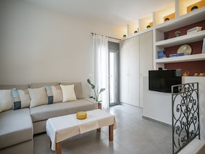 A modern living room with a sofa, a coffee table, a TV, and a bookshelf. - Elegant City Apartment - 250m From Solomos Square (Zakynthos)