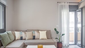 A living room with a beige sofa, a small table with a glass bowl, and a potted plant. - Elegant City Apartment - 250m From Solomos Square (Zakynthos)