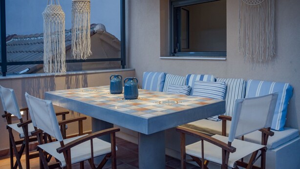 An outdoor seating area with a checkered table, cushioned chairs, macrame hangings, and a view of the rooftops. - Elegant City Apartment - 250m From Solomos Square (Zakynthos)