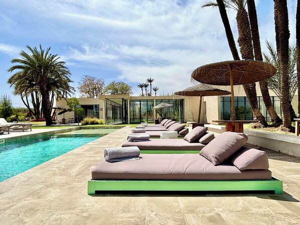 A poolside area with lounge chairs and a glass-enclosed structure. - Palais Akbal (Marrakech)